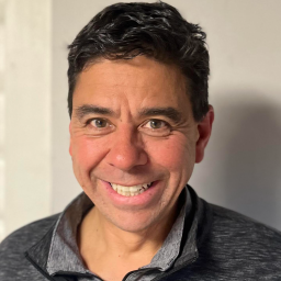 Brian Bauer smiling standing in front of a beige wall.
